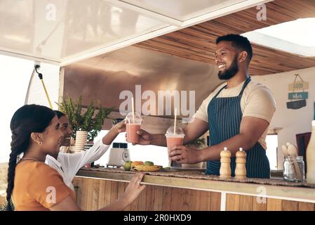 Ich hoffe, es gefällt Ihnen, Ladys. Zwei Freunde, die mit dem Besitzer eines Food Trucks sprechen, während sie Smoothies kaufen. Stockfoto