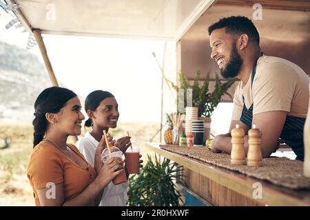 Verbreiten Sie die Botschaft weit und breit. Zwei Freunde, die mit dem Besitzer eines Food Trucks sprechen, während sie Smoothies kaufen. Stockfoto