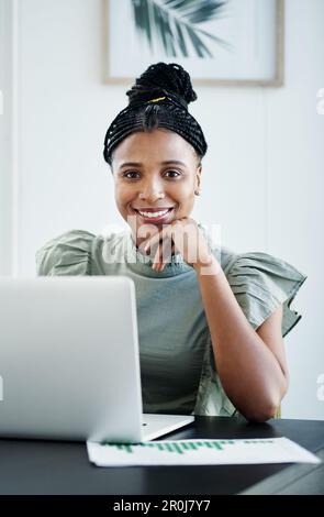 Ich arbeite ständig an meinem Geschäftsplan. Eine attraktive junge Geschäftsfrau, die allein in ihrem Büro sitzt und ihren Laptop benutzt. Stockfoto