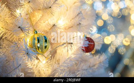 Hängende Bälle auf weißem Baum mit hellem Bokeh-Hintergrund. Weihnachtskonzept. Stockfoto