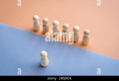 Eine Holzpuppe, die einer Reihe von Puppen gegenübersteht, die durch verschiedene Farben voneinander getrennt sind. Führungskonzept. Stockfoto