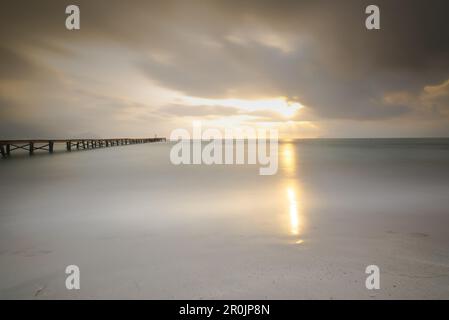 Lange Sicht auf einen hölzernen Pier am Strand Playa de Muro in Morgenstimmung. Der Himmel ist bedeckt und Nebel liegt über der Bucht von Alcudia, Alcudia, Mallorca Stockfoto