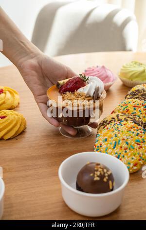 Serviertisch mit exquisiten Desserts, dazu Tasse mit Eiscreme, Sahne und Erdbeere, kongeösen Plätzchen und Schokoladenball, appetitlich Stockfoto