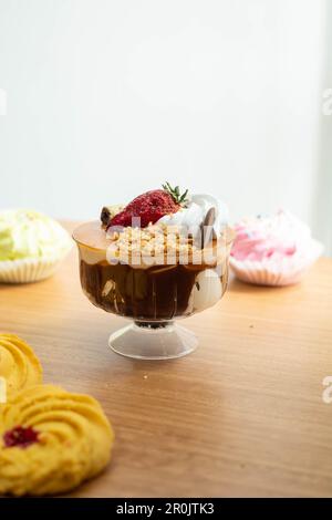 Leckere Tasse mit Eis, Sahne, Erdbeeren im Hintergrund Kekse, süße Desserts auf dem Studiotisch als Tapete, Gebäck und Süßwaren Stockfoto