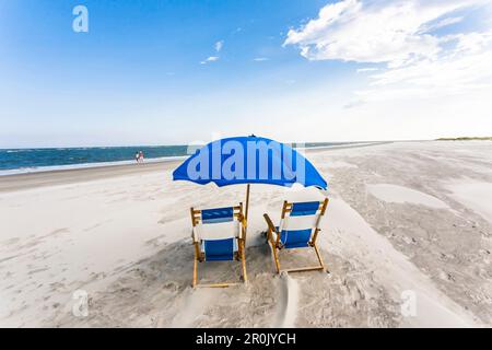 2 Liegestühle und ein Sonnenschirm in Blau sind ein einsamer Ort am weitläufigen Strand der Isle of Palms, Charleston, South Carolina, USA Stockfoto