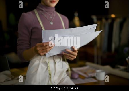 Die Nahaufnahme einer professionellen, Millennials asiatischen Schneiderin oder Modedesignerin konzentriert sich darauf, ihre Modellskizzen in ihrem Studio zu überprüfen. Stockfoto