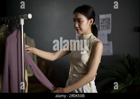 Wunderschöne junge asiatische Modedesignerin, die ihre neue Kollektion überprüft, in ihrem Studio arbeitet. Stockfoto