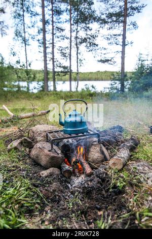 Wasserkocher aus blauem Emaille steht auf einem Gitter auf einem Lagerfeuer in der Nähe eines kleinen Sees, Varmland, Schweden Stockfoto