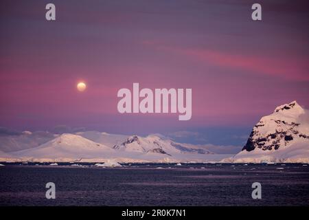 Vollmond über schneebedeckten Bergen in der Dämmerung nahe Lemaire Channel, Graham Land, Antarktis-Halbinsel, Antarktis Stockfoto