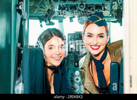 Schöne Frau Pilot trägt Uniform. Glücklicher und erfolgreicher Flug. Blick auf die Kamera in der Ebene. Mädchen, die die Kamera betrachten. Zwei Piloteninnen sitzen darin Stockfoto