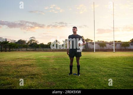 Ich behalte meine Sportziele im Auge. Die lange Aufnahme eines gutaussehenden jungen Sportlers, der alleine steht und einen Rugbyball hält, bevor es früh morgens losgeht Stockfoto