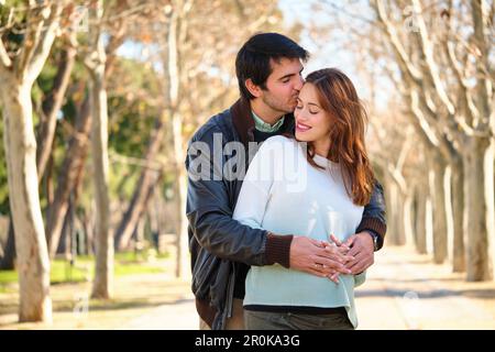 Ein Mann küsst seine glückliche schwangere Frau, ein Paar umarmt einen Park. Stockfoto