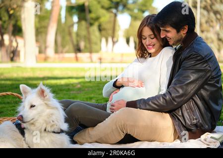 Glückliches schwangeres Paar, das mit seinem Hund ein Picknick macht. Stockfoto