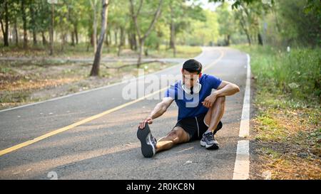 Fit und sportlich der Asiate der Millennials streckt sich auf der Straße die Beine und wärmt sich vor dem Laufen auf. Stockfoto