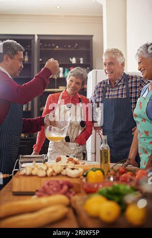 Kochen, Essen und Seniorenfreunde in der Küche eines Hauses für eine Dinnerparty oder eine gesellschaftliche Feier. Diversität, Ruhestand oder Gemeinschaft mit einem Stockfoto