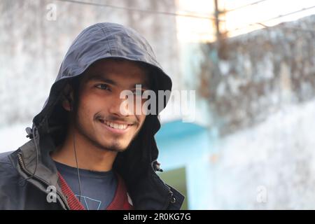 Ein junger, schöner Junge, der in Portrait lächelt. Er trägt Kapuzenpullover, sieht draußen in die Kamera. Stockfoto