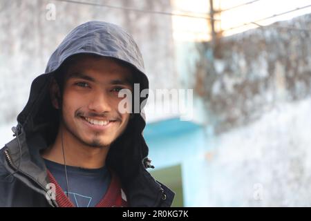 Ein junger, schöner Junge, der in Portrait lächelt. Er trägt Kapuzenpullover, sieht draußen in die Kamera. Stockfoto