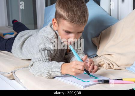 Das Kind malt mit Filzstiften, die auf dem Boden liegen, auf Papier. Kind, das zu Hause Schulunterricht nimmt. Kindererziehungskonzept, Kid Boy Drawing und Dreaming S. Stockfoto