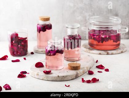 Hausgemachtes Rosenwasser oder Sirup in Glasflaschen für die Zubereitung von Cocktails, Getränken, Limonade oder süßen Desserts. Gesundes Sommeressen Konzept. Stockfoto