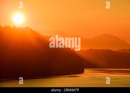 Die goldene Sonne erhebt sich hinter den Bergen, die vom Expeditionsschiff MS Bremen (Hapag-Lloyd Cruises), Milbanke Sound, Inside Passage, zwischen Denny, aus gesehen werden Stockfoto