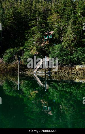 Ein von Bäumen umgebenes Grünhaus und ein Pier spiegeln sich in den ruhigen Gewässern von Elfin Cove, Elfin Cove, Chichagof Island, Alaska, USA, Nordamerika Stockfoto