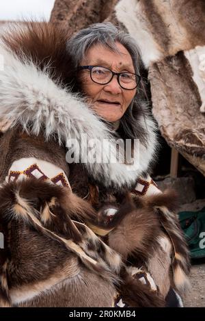 Eine ältere Frau mit Brille und traditioneller Pelzkleidung sitzt vor einem Rentierfell-Tipi, Gjoa Haven, King William Island, Nunavut, Kanada, N Stockfoto