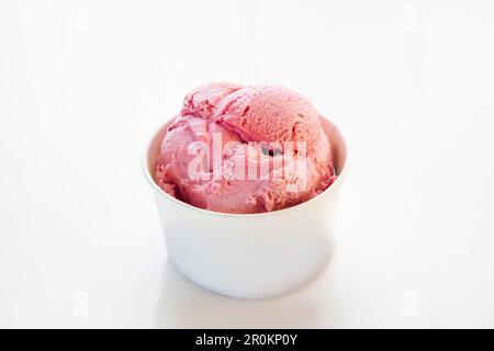 Erdbeereis in einem Pappbecher mit transparentem Plastiklöffel. Stockfoto