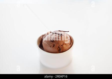 Belgisches Schokoladeneis in einer weißen, markenlosen Tasse serviert mit einem durchsichtigen Plastiklöffel. Stockfoto