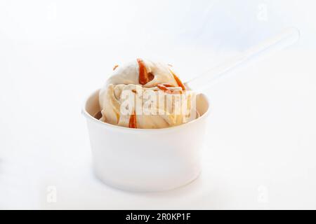 Vanille-Karamell-Eiscreme aus weißer Schokolade in einem Pappbecher ohne Markenkennzeichnung mit Plastiklöffel. Stockfoto