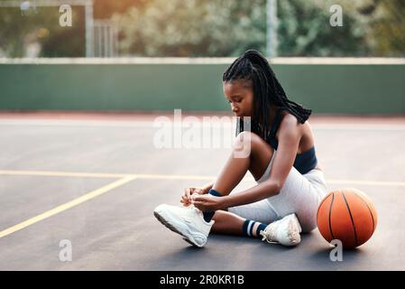 Ich Sorge dafür, dass meine Schnürsenkel eng sind. Eine attraktive junge Sportlerin, die auf dem Platz sitzt und ihre Schnürsenkel bindet, bevor sie Basketball spielt. Stockfoto