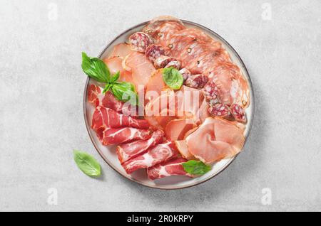 Servierplatte mit geräuchertem Fleisch, Antipasto-Set, Vorspeise auf Teller auf grauem Betonhintergrund Stockfoto