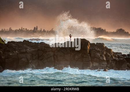 HAWAII, Oahu, North Shore, Individuen auf den Felsen, die die Surfer am Außenpunkt der Waimea Bay vom Pupukea Beach Park aus sehen Stockfoto