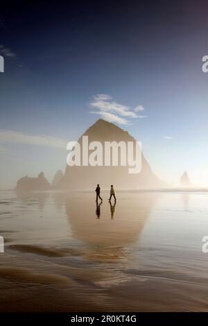 USA, Oregon, Pacific City, Individuen spazieren am Pacific City Beach entlang, wobei Haystack Rock in der Ferne liegt Stockfoto