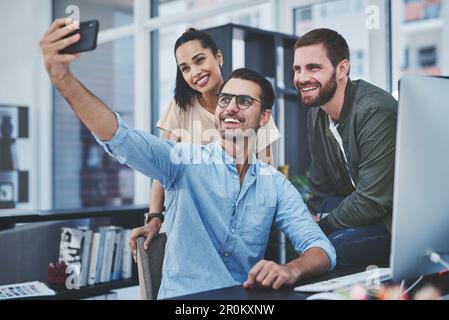 Nehmen wir einen für unsere Website. Eine Gruppe von Designern, die Selfies zusammen in einem Büro machen. Stockfoto