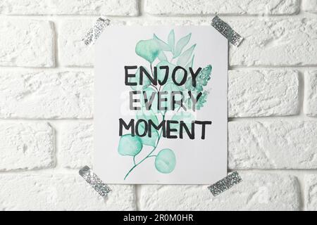 Karte mit Text Genießen Sie jeden Moment an der weißen Backsteinwand Stockfoto