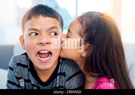Jetzt reicht's mit den Küssen. Ein bezauberndes kleines Mädchen küsst zu Hause ihren großen Bruder auf die Wange. Stockfoto
