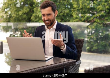 Ein glücklicher bärtiger Mann, der sich im Café im Freien per Video unterhält Stockfoto