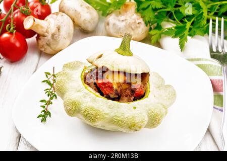 Patisson gefüllt mit Leber, Zwiebeln, Pilzen, Tomaten und Käse auf einem Teller, Handtuch, Champignons und Petersilie auf Holzbretthintergrund Stockfoto