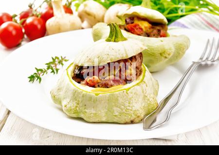 Zwei Kürbisse gefüllt mit Leber, Zwiebeln, Pilzen, Tomaten und Käse auf einem Teller, Handtuch, Champignons und Petersilie auf Holzbretterhintergrund Stockfoto