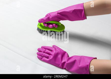 Frau in lila Handschuhen, die weiße Matratze mit Bürste reinigt, Nahaufnahme Stockfoto