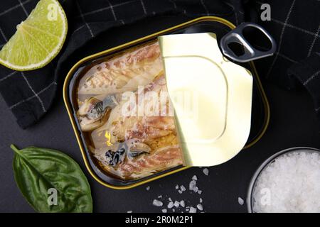 Offene Blechdose mit Makrelenfilets und Gewürzen auf schwarzem Tisch, flach liegend Stockfoto