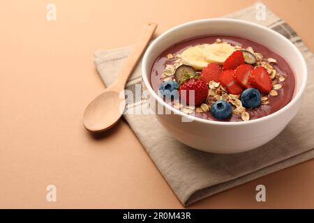 Köstliche Smoothie-Schüssel mit frischen Beeren, Banane und Müsli auf blassorangefarbenem Hintergrund. Platz für Text Stockfoto