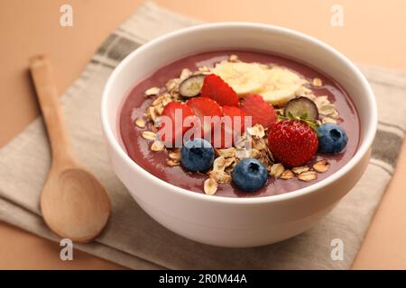 Köstliche Smoothie-Schüssel mit frischen Beeren, Banane und Müsli auf blassorangefarbenem Hintergrund, Nahaufnahme Stockfoto