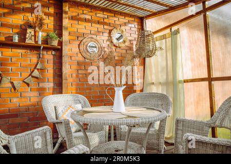 Terrasse im Boho-Stil mit Vorhängen und Korbmöbeln, Rattan und Schilf. Wand aus Gewächskunststoff und Decke aus Polycarbonat. Stockfoto