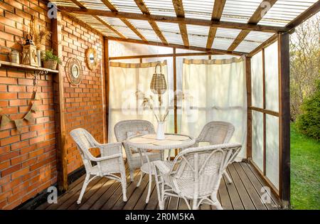 Terrasse im Boho-Stil mit Vorhängen und Korbmöbeln, Rattan und Schilf. Wand aus Gewächskunststoff und Decke aus Polycarbonat. Stockfoto