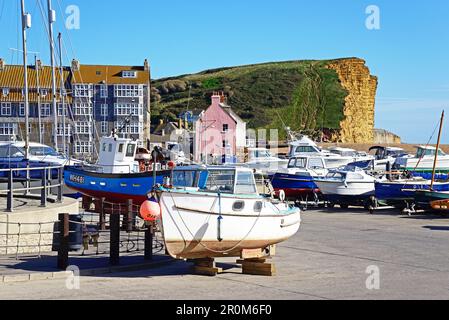 Boote im Trockendock entlang des Promenadenpiers mit Blick auf den Kieselstrand und die Klippen der Jurassic Coast, West Bay, Dorset, Großbritannien. Stockfoto