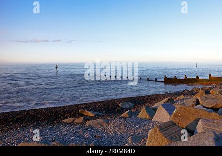 Strand mit Felsgepanzerung und holzhaltiger Wellenbrecherseeabwehr an der Nordnorfolkküste in Sheringham, Norfolk, England, Großbritannien. Stockfoto