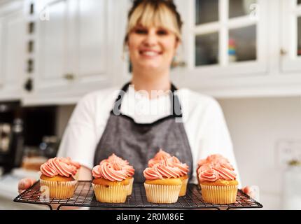Auch Sie können Ihre Liebe zum Backen in ein Heimgeschäft verwandeln. Eine Frau, die zu Hause frisch gebackene Cupcakes in der Küche hält. Stockfoto