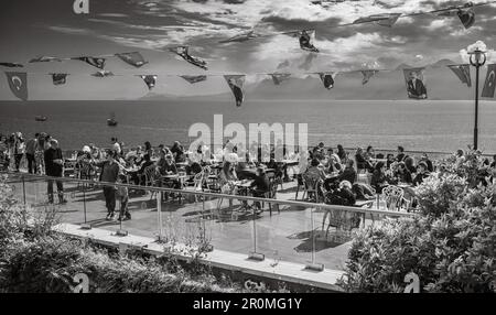 Die Menschen sitzen unter nationalistischen Flöten und genießen den Panoramablick auf die Bucht und den Hafen von einem Café im Freien, das sich an den antiken Stadtmauern befindet Stockfoto