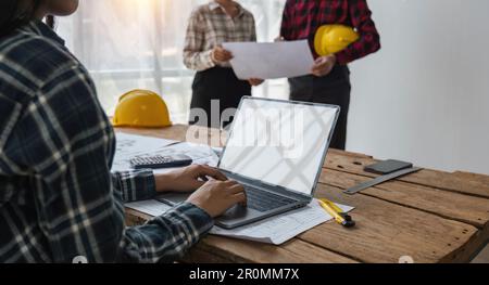 Ein Team von Bauingenieuren, die im Büro arbeiten und sich einen Laptop ansehen, um den Entwurf des Gebäudeplans zu besprechen Stockfoto